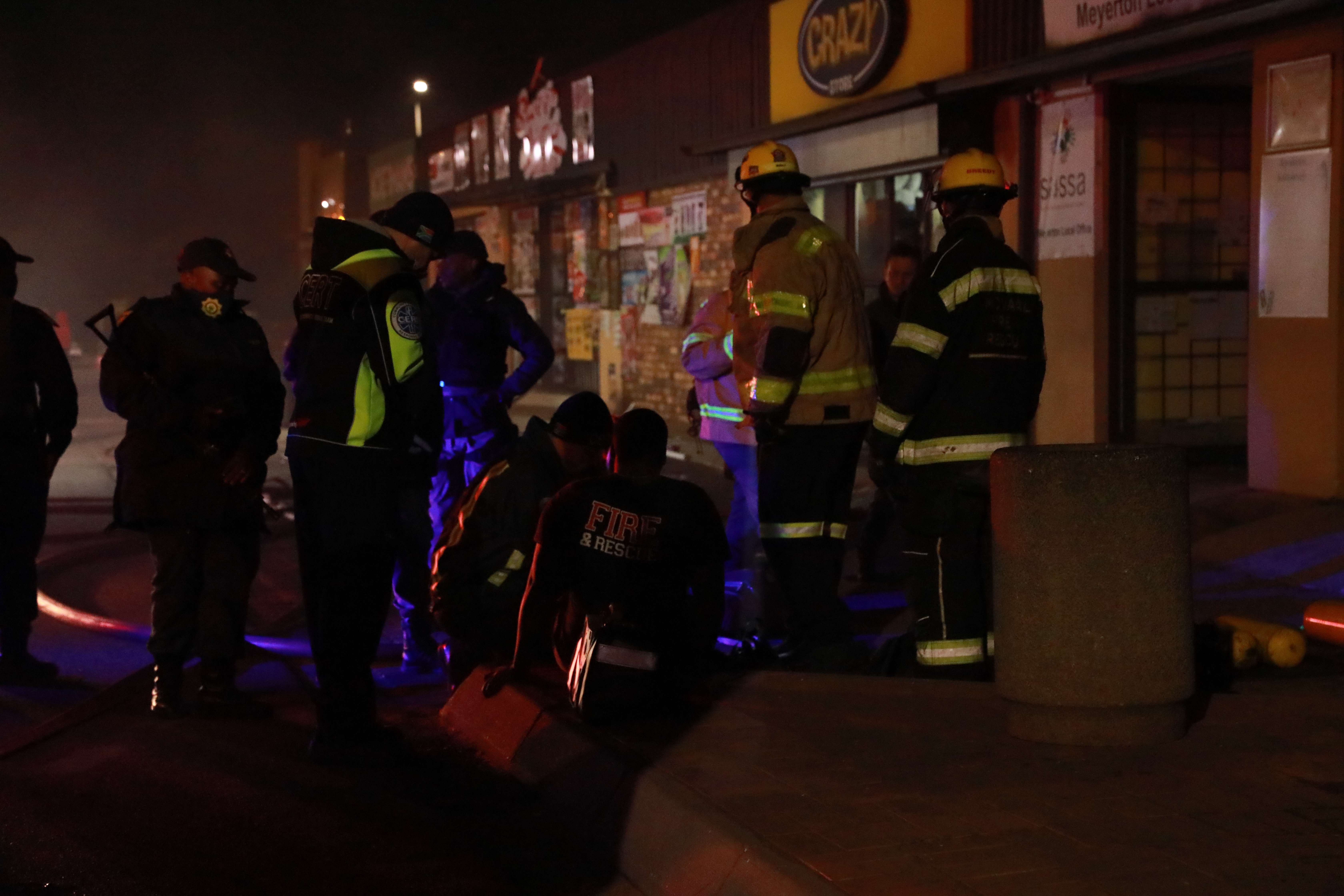 Fire and Rescue personnel, SAPS officers and emergency workers gathered outside the Crazy Store and SASSA Meyerton Local Office during the commercial block fire on 21 July 2026