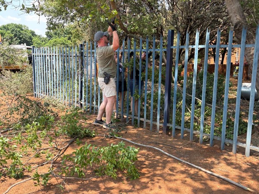 Volunteer trimming overhanging branches along the police station fence